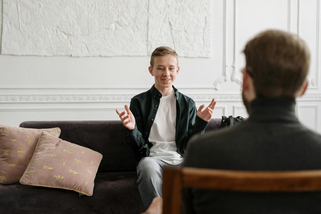 Teen in discussion with therapist on a sofa during a counseling session indoors.