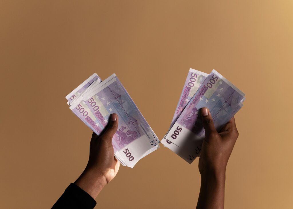 Close-up image of hands holding 500 euro banknotes on a neutral beige background.